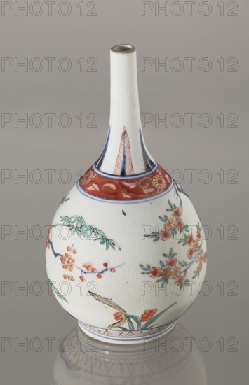 Bottle, decorated in the kakiemon style with a motif of the three friends of winter bamboo, plum, and pine; rock. Also decorated with two borders with plant motifs and floral patterns on the neck. Early 18th century, Edo period 1603–1868, Japan. Porcelain vessel sake bottle, height 22.1 cm, diameter 12 cm. Materials: ceramics, porcelain. Subjects/ornament: bamboos, pines, plums, plant ornament, Imari influence., A ceramic bottle with a long narrow neck and rounded body sits against a neutral gray background, decorated with painted floral and bamboo motifs in colors including white, red, green, blue, orange, yellow, and a touch of brown; the neck is predominantly white with blue accents near its base and a red band with floral patterns encircling the shoulder, and the body shows a group of delicate blossoms and leafy branches in green and orange with blue stems and small yellow details, plus a painted blade-like leaf near the base; the surface has visible crackle lines and a reflective ...