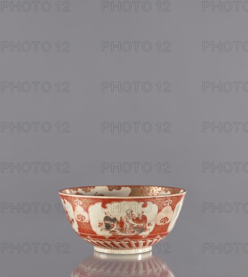 Bowl, Kutani, 19th century Edo period, Japan Kaga. Porcelain vessel, height 8.8 cm, diameter 18.8 cm. Decoration: figural scenes, birds, flowers, plum trees, chrysanthemums—kacho/kachôga flowers and birds., A shallow ceramic bowl sits on a reflective surface against a plain gray background, showing a palette of red, off-white, cream, and touches of brown and gold. The bowl's exterior features decorative panels with painted human figures and ornamental cloud-like motifs in red on an off-white ground, with a red band near the rim and a patterned red and cream base. The interior rim displays red and gold decorative elements and the glaze shows a slightly crackled texture. The reflection beneath the bowl repeats its red and cream pattern on the smooth surface.