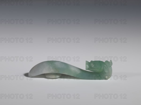 Belt clasp, Chinese, Chinese art; dragons iconography; Qing 1644–1911; clothing — belts, men's clothing, costumes, ornaments, men's ornaments; smooth handle. Green-gray jadeite, semi-transparent with slight colloid clusters. Full-plastic carved head. 17th–18th century, China. Belt buckle; height 2.0 cm, width 9.1 cm, depth 1.7 cm., A smooth carved object rests on a flat surface, appearing translucent with gradients of green and pale green blending into grayish tones; the form curves like an elongated loop with one end raised and detailed into a rounded head with subtle carved features, while the underside shows a small circular support piece.
