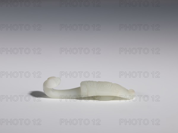 Belt clasp, Chinese, Chinese art, cicadas, lizards, Qing 1644–1911. Stem: stylized cicada with a geometric meander motif. Milky-white jadeite, slightly translucent visible clusters of colloids. Head carved in full relief; flat relief. 17th–18th century, China. Belt buckle. Height 1.8 cm; width 8.0 cm; depth 2.1 cm., A smooth pale off-white carved object shaped like a stylized animal with a curved neck and rounded head sits on a flat surface, casting a soft shadow; the body is elongated and slightly raised with subtle carved geometric and spiral patterns visible on its back; the scene shows a gradient background transitioning from darker gray at the top to very light gray near the surface, and the visible colors are off-white, pale cream, gray, and shadowed tones of blackish gray.
