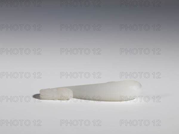 Belt clasp, Chinese, dragons iconography, Qing 1644–1911, handle devoid of engraved decoration, polished smoothly, milky-white jadeite, slightly translucent, full-plastic carved head, engraved, 18th–19th century, China, belt buckle, height 1.5 cm, width 8.8 cm, depth 1.7 cm, A smooth, elongated pale-white object rests horizontally on a flat white surface, casting a soft shadow beneath it; one end of the object tapers into a carved section with subtle engraved patterns and rounded features, while the opposite end is bulbous and gently rounded. The scene shows shades of white, off-white, and light gray, with a gradient gray background fading darker toward the top.