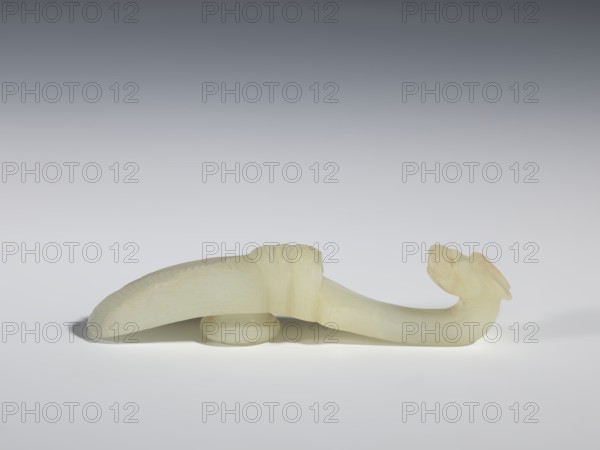 Belt clasp, Chinese, Qing dynasty 1644–1911, 18th–19th century. Milky-white translucent jade. Shaft in flat relief; head carved in full relief. Iconography: cicadas and dragons. Belt buckle; height 2.4 cm, width 10.7 cm, depth 2.1 cm., A pale, translucent carved object rests on a smooth surface against a gradient gray background, appearing to be made of a creamy off-white material with subtle yellowish tones; the form includes a curved, elongated body with a rounded base support and a hooked, stylized head at one end, the main curved section showing carved ridges and textured patterns along its upper edge and smooth areas along its underside, casting a soft shadow on the surface beneath.