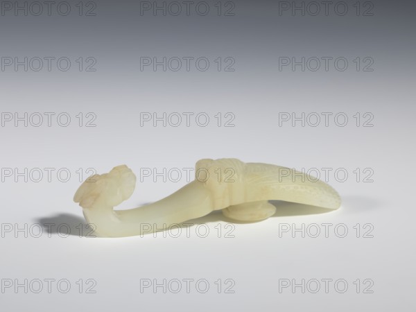 Belt clasp, Chinese art, Qing style Qing dynasty, 1644–1911, Chinese, iconography: cicadas and dragons; milky-white translucent jade; shaft in flat relief, head carved in full relief; 18th–19th century, China; belt buckle; height 2.4 cm, width 10.7 cm, depth 2.1 cm., A pale, smooth carved object in shades of off-white and cream rests on a light gray surface, casting a soft shadow; the carving features a curved elongated form with a bulbous decorative end and a flattened, textured section with carved dots and ridges, showing subtle variations of cream and very light yellow, with faint beige accents.