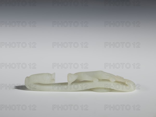 Belt clasp, Chinese culture, dragons iconography, lizards zool., Qing 1644–1911. The head is in the shape of a two-horned dragon's head with an open mouth, and the handle features a lizard. Milky-white jadeite, slightly translucent with slight colloid clusters. Carving, engraving; 18th–19th century, China. Belt buckle; height 2.1 cm, width 12.8 cm, depth 2.2 cm., A pale, creamy white carved object rests on a smooth surface against a gradient gray background, shaped like a long, sinuous form with rounded ends and subtle raised details suggesting limbs and facial features, casting a soft shadow beneath it; the overall visible colors are creamy white, light gray, and darker gray in the background.