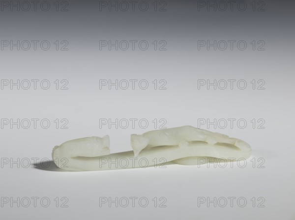 Belt clasp, Chinese, Qing dynasty 1644–1911. 18th–19th century. Milky-white jadeite, slightly translucent with slight colloid clusters. Carving and engraving. The head is in the shape of a two-horned dragon's head with an open mouth, and the handle features a lizard. Belt buckle. Height 2.1 cm, width 12.8 cm, depth 2.2 cm. Dragons; lizards., A pale, smooth carved object with an elongated, looping form rests on a flat surface, showing a few rounded protrusions and curved, tapered ends; the object appears translucent and off-white with subtle variations in lightness. The background is a gradient from dark gray at the top to light gray near the middle and white at the bottom, and there is a soft shadow beneath the object.