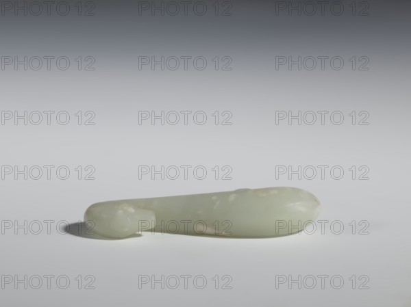 Belt clasp, Chinese, Qing 1644–1911, 17th–18th century. Milky-white slightly translucent jadeite, smooth rounded handle. Full-sculpture carved lizard head, engraved. Belt buckle. Height 2.2 cm, width 10.5 cm, depth 2.1 cm., A smooth, elongated object rests horizontally on a flat surface, appearing to be made of a pale, translucent material in shades of light green and off-white with some faint cloudy patches. The object has rounded ends, one end slightly bulbous and the other tapering to a smaller rounded tip, and it casts a soft shadow on the surface beneath it. The background transitions from a darker gray at the top to a lighter gray near the surface, and the overall lighting is soft and diffuse, highlighting the object's glossy surface and subtle color variations.