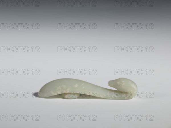 Belt clasp, Chinese, Qing dynasty 1644–1911, 17th–18th century. Milky-white, slightly translucent jadeite; smooth, rounded handle. Full-sculpture carved head with engraved details depicting lizards. Belt buckle; height 2.2 cm, width 10.5 cm, depth 2.1 cm., A smooth pale greenish-white carved object shaped like a stylized animal with a rounded head at one end and a gently curved elongated body, resting on a flat surface with a soft shadow; colors visible include pale green, white, and subtle creamy off-white mottling, set against a neutral light gray to darker gray gradient background.