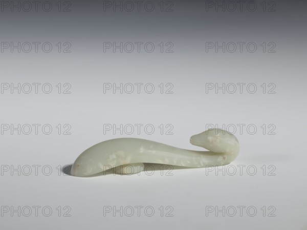 Belt clasp, Chinese, lizards, Qing 1644–1911. Smooth, rounded handle. Milky-white slightly translucent jadeite. Full-sculpture carved head, engraved. 17th–18th century, China. Belt buckle. Height 2.2 cm; width 10.5 cm; depth 2.1 cm., A smooth, pale green object resembling a curved animal form rests on a light surface, showing subtle cloudy patches of lighter and slightly cream tones; the object has a rounded, elongated body that tapers into a thicker, rounded head shape and casts a soft shadow beneath it, with the background gradient shifting from light gray near the surface to darker gray toward the top.