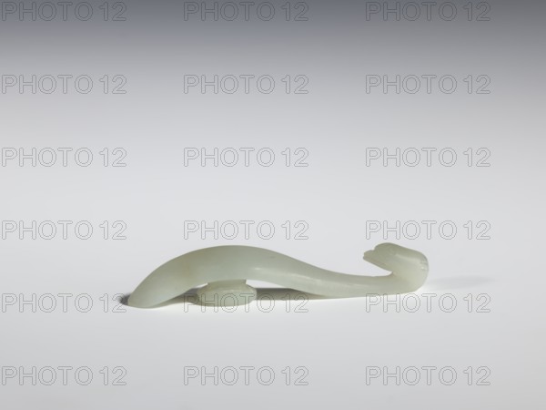 Belt clasp, Chinese, Chinese art; birds; Qing dynasty 1644–1911; 17th–18th century; milky-white jadeite with slightly green tint, clusters of colloids; full-sculpture carved head; handle with an edge on the spine and a pointed tip; belt buckle; height 1.3 cm, width 7.3 cm, depth 0.96 cm., A smooth pale green, translucent curved object resembling a stylized animal form rests on a pale gray surface; it has a rounded body that tapers into a slender neck and head with subtle carved features, supported near its underside by a small rounded base, and casts a soft shadow on the surface, with colors visible including pale green, light gray, and hints of white.