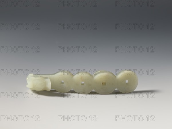 Belt clasp, Chinese, Chinese art, coins, dragons iconography, Qing 1644–1911. Shaft: four connected Chinese coins. Milky-white jadeite with a slightly green tint. Full-plastic carved head, engraved, early 20th century, China. Belt buckle; height 2.4 cm, width 11.3 cm, depth 2.3 cm., A pale, translucent object with a smooth, slightly glossy surface rests horizontally on a neutral background. The object consists of a connected series of round discs with square holes at their centers, transitioning into a carved end that has a rounded, slightly organic shape. The material appears off-white to creamy with faint variations in tone, and there are subtle shadows beneath and behind the object that appear gray. The background shows a gradient from darker gray at the top to lighter gray and near-white toward the bottom.
