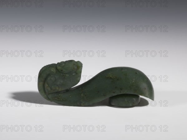 Belt clasp, purchased provenance, Chinese, dragons iconography, Qing 1644–1911, clothing, belts, men's clothing, costumes, ornaments, men's ornaments, buckles, spinach jade, uniformly colored, full-plastic carved head, engraving, bas-relief, 18th–19th century, China, belt buckle; height 3.5 cm, width 9.5 cm, depth 3.1 cm., A smooth carved object made of dark green stone with lighter green and brown mottling sits on a white surface against a gray gradient background; the carving features a curved, elongated body that rises into a rounded head with subtle carved facial and decorative details, and a small rounded base piece partially visible beneath the larger form, casting soft shadows on the surface.