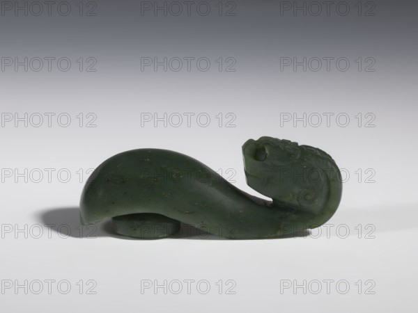 Belt clasp, Chinese, dragons iconography, Qing 1644–1911, men's clothing/ornaments, buckles, spinach jade, uniformly colored, full-plastic carved head, engraving, bas-relief, 18th–19th century, China, belt buckle; height 3.5 cm, width 9.5 cm, depth 3.1 cm., A carved object in dark green with lighter green and small brownish flecks rests on a light surface against a gradient gray background; the object has a smooth, curved body that rises and tapers toward one end where a carved head with rounded features and shallow carved patterns is visible, and a small rounded support piece sits beneath the body, casting a soft shadow on the surface.