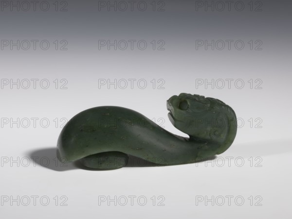 Belt clasp, Chinese, dragons iconography, Qing 1644–1911, clothing, belts, men's clothing, costumes, ornaments, men's ornaments, buckles, spinach jade, uniformly colored, full-plastic carved head, engraving, bas-relief, 18th–19th century, China, belt buckle, height 3.5 cm, width 9.5 cm, depth 3.1 cm, A carved dark green stone object shaped like a stylized animal form with a curved body and an upturned head, showing carved facial features and surface detailing; the stone has small darker flecks and a slightly glossy finish, and the piece rests on a smooth light-gray surface with a soft shadow beneath and a gradient gray background.