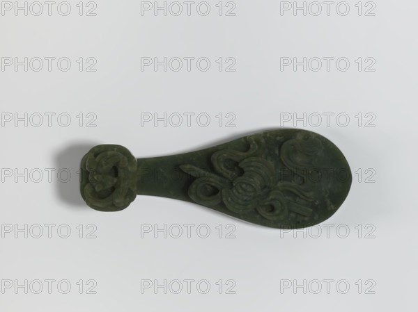 Belt clasp, Chinese, Chinese art, lizards zool., ruyi auspicious scepter iconographic, Immortals iconographic, Taoism, Qing 1644–1911. Scepter head with a bas-relief stylized lizard, shaft with a Taoist emblem of one of the Eight Immortals. Spinach jade. Sculpture, engraving, 18th–19th century, China. Belt buckle. Height 2.7 cm; width 12.0 cm; depth 4.5 cm., A dark green carved object with a rounded teardrop-shaped body and a squared handle, featuring raised curving decorative patterns on its surface; the carving shows a few flowing, spiral-like motifs and some textured areas. The background is a smooth light surface in shades of white and pale gray, and there is a soft shadow beneath the object in muted gray.