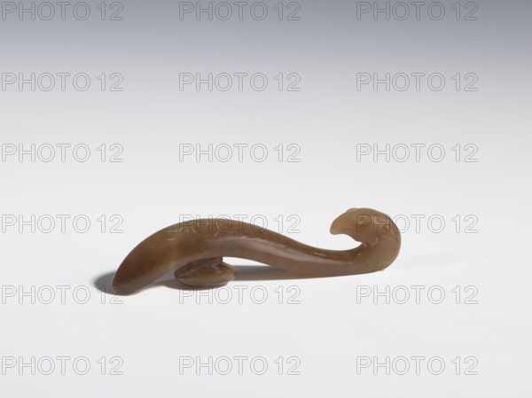 Belt clasp, purchase provenance; Chinese; Qing dynasty 1644–1911; brown jade with lighter spots; full-plastic carved head; engraved; 18th–19th century; China; motifs: birds, phoenixes, dragons; belt buckle; height 1.6 cm, width 7.4 cm, depth 1.2 cm., A small carved object with a smooth curved form resembling a hooked shape, brown in color with slightly lighter and darker brown variations, resting on a white surface with a soft gray gradient background; the object has a rounded end and a hooked end that suggests a beak-like curve, with a few subtle carved lines and a small rounded support piece beneath the middle that casts a soft shadow.