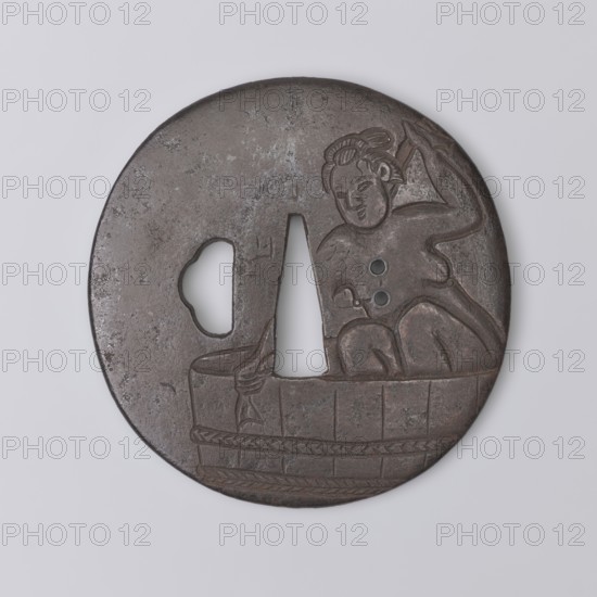 Crossguard tsuba, Yoriie,  ; engraved decoration depicting a naked woman bathing in a large tub and wiping her back with a towel; on its body, where the kôgai hitsu ana is usually located, there are two holes udenuki ana. . Images of women; sword crossguard; Japanese art; Japanese culture; Edo 1603–1868; weapon; melee weapon; katana; woman iconography; nudity; swords; round tsuba maru gata; katahitsu ana; rounded edge maru mimi. 18th century Edo period, 1603–1868, Japan. Tsuba; diameter 7.7 cm; thickness 0.3 cm., A round metal object with a dark brown and gray patina shows a carved depiction of a seated figure with stylized hair and a raised arm, positioned above a carved barrel or tub with decorative bands; the object has a central triangular cutout and an irregular shaped hole to one side, and the surface displays areas of darker brown, lighter gray, and mottled black.