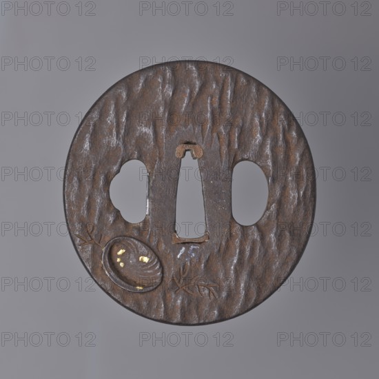 Crossguard tsuba, Tsuchiya,  school author, Enjusai Kanri, / personal slogans / creator, Japanese art, Japanese culture, Edo 1603-1868, weapons, melee weapons, swords, katana, sword crossguards, shells, Oval tsuba tatemaru gata with a rectangular edge kaku mimi and a surface textured by hammering, decorated in high, inlaid relief taka-zôgan with a motif of shells and aquatic plants engraved plants. Decoration details accentuated with gold inlay., 18th century Edo period 1603-1868, Japan type of place / place of origin, Edo now Tokyo, tsuba, height 7.1 cm, width 6.9 cm, depth 0.9 cm, A round metal object with a textured, mottled surface in shades of brown and dark gray, showing a few irregularly shaped cutouts including a central vertical slot and two rounded openings on either side; the surface has a rough, hammered appearance with subtle highlights of lighter gray and small areas of gold-colored inlay within a shallow oval depression near the lower left, along with incised, branchlike...