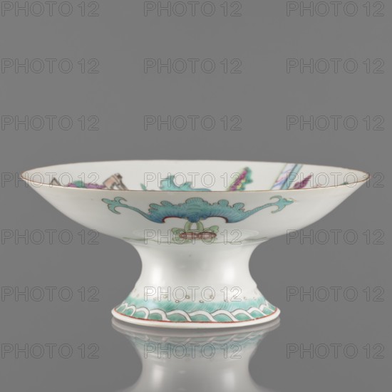 Platter, Paderewski, Ignacy Jan 1860–1941. Chinese art; Qing dynasty Tongzhi, 1862–1874. Porcelain platter with white transparent glaze, decoration painted with overglaze enamels and iron red, gilded edge. Subject: go game, figural scenes of women, scholars, musical instruments. Vessel; height 8.5 cm, diameter 21 cm; dated 1862–1874; China., A shallow white porcelain footed bowl with a wide flared rim decorated with painted ornamental motifs in turquoise, teal, green, pink, purple, and gold, showing a central stylized floral or cloud-like design on the exterior and a patterned band around the pedestal base, set against a neutral gray background with a soft reflection beneath.
