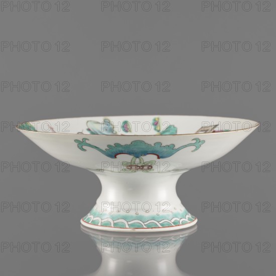 Platter, gift; Paderewski, Ignacy Jan 1860-1941; Chinese art; Chinese; Qing dynasty 1644–1911, Tongzhi period 1862–1874; ceramics; colored porcelain; subject: go game, figural scenes, images of women, scholars, musical instruments; porcelain platter with white, transparent glaze; decoration painted with overglaze enamels and iron red, gilded edge; 1862–1874; China; vessel; height 8.5 cm; diameter 21 cm, A shallow pedestal bowl photographed against a plain gray background, with a white porcelain surface and decorative motifs in turquoise, green, red, and gold; the bowl has a flared rim with a thin gold edge, a concave interior showing small painted floral and ornamental elements in turquoise and green, and an outward scrolling turquoise motif on the exterior above a small stylized floral device in pale green and red; the pedestal foot is white with a band of turquoise wave-like decoration and small gold dots above a thin red line at the base, and the bowl and its foot are reflected fain...