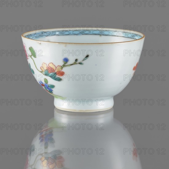 Bowl. Porcelain with white, transparent glaze with bluish tint; decoration painted with overglaze enamel paints. Spherical bowl form. 19th century Qing dynasty, 1644–1911. China. Colored porcelain. Height 5.5 cm; diameter 8.8 cm. Subject: flowers., A small white porcelain bowl with a rounded body and narrow foot, decorated on the exterior with a painted floral branch featuring petals and leaves in colors including green, blue, pink, orange, and yellow, with delicate dark green stems and small dark accents; the rim has a thin golden band and an inner border in light blue with a crosshatch pattern, and the bowl sits on a reflective gray surface that creates a blurred mirror image of the painted flowers.