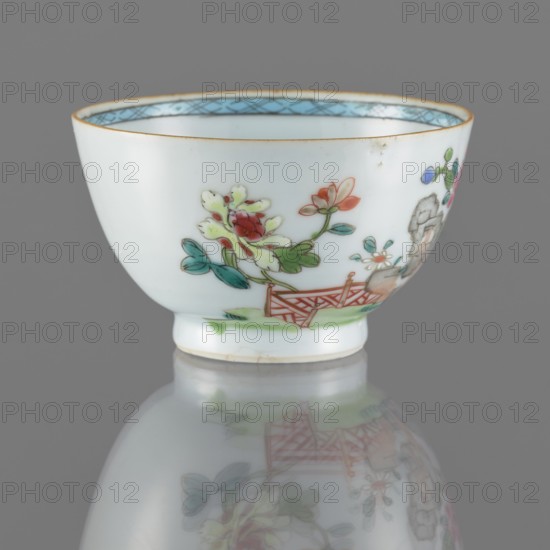 Bowl. Porcelain with white, transparent glaze with a bluish tint; decoration painted with overglaze enamel paints. Spherical bowl form. 19th century Qing dynasty, 1644–1911. China. Colored porcelain; Chinese style. Height 5.5 cm, diameter 8.8 cm. Subjects: flowers., A small white porcelain cup with a rounded body and short foot sits on a reflective grey surface, decorated with painted floral motifs including blossoms in red, pink, and pale yellow with green leaves and teal accents, a small stylized fence in orange-red, and touches of blue and pale turquoise along the interior rim; the cup shows a thin gold rim and a few tiny surface imperfections, and its painted decoration and colors are reflected softly beneath it.