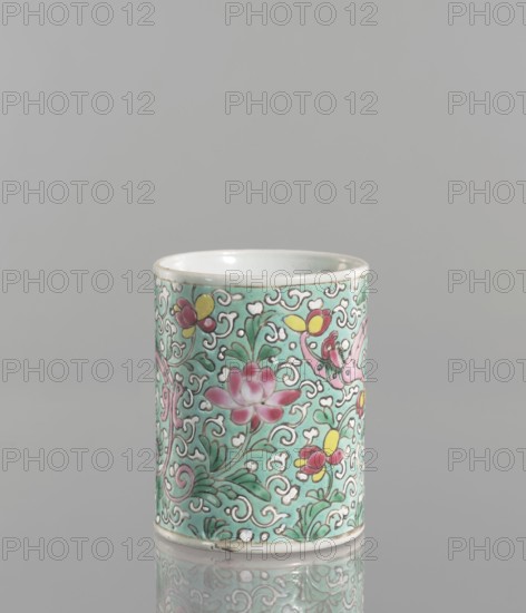 Brush vessel. Chinese, Qing dynasty 1644–1911, 19th century. Porcelain fragment with celadon glaze; decoration painted with overglaze enamel paints. Cylindrical brush vessel with floral tendril and dragons iconography. Height 12.1 cm; diameter 9.6 cm; weight 0.5 kg., A cylindrical ceramic cup with a glossy pale green background covered in a swirling floral pattern, showing a group of pink lotus-like blossoms, several yellow and red flower buds, and green leaves outlined in darker lines, all set among white cloud-like scroll motifs; the rim and base are white with a thin darker edge, and the cup sits on a reflective gray surface with a plain light gray background.