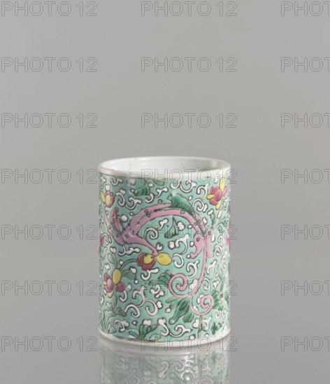 Brush vessel. Chinese; Qing dynasty 1644–1911. Porcelain with celadon glaze; decoration painted with overglaze enamel paints. Cylindrical brush vessel decorated with floral tendril and dragons. 19th century. Height 12.1 cm; diameter 9.6 cm; weight 0.5 kg., A cylindrical ceramic cup with a smooth white rim and base sits against a neutral gray background, its exterior covered in an intricate floral and scroll pattern in green, pink, yellow, white, and touches of red, with several leafy shapes and curling vine-like designs wrapping around the surface and a reflective surface beneath creating a faint mirrored image.