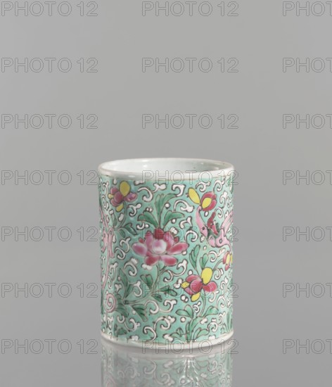 Brush vessel, Chinese, Qing 1644–1911, 19th century. Porcelain fragment with celadon glaze; decoration painted with overglaze enamel paints depicting floral tendrils and dragons. Cylindrical colored-porcelain brush vessel. Height 12.1 cm; diameter 9.6 cm; weight 0.5 kg., A cylindrical ceramic cup sits upright on a reflective surface, showing a decorative exterior with a turquoise background and an intricate raised pattern of swirling white lines. The surface is adorned with floral motifs in pink and yellow with green leafy stems, and a few stylized bird-like elements in pink. The rim and base are white, and the interior appears pale with a glossy finish. The overall color palette includes turquoise, pink, yellow, green, white, and subtle gray reflections.