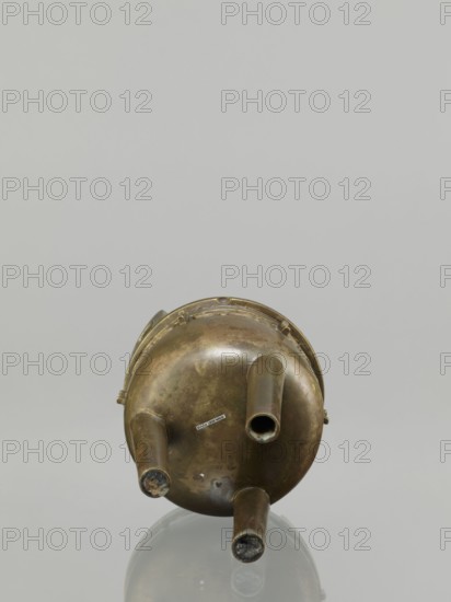 Ding incense burner, leiwen ornament, Chinese art, Ding vessel, Chinese culture, ceremonial/ritual vessel, decorative birds motif, meander ornament, Qing dynasty 1644–1911, 19th century, China, vessel, height 19.2 cm, diameter 13.6 cm, A metallic, round, aged object with a patina of brownish bronze and greenish tarnish sits upright on a reflective surface, showing a rounded base with three tubular protrusions extending outward; the metal has darker and lighter patches and some worn areas, and the reflection and neutral background display shades of gray and muted silver.