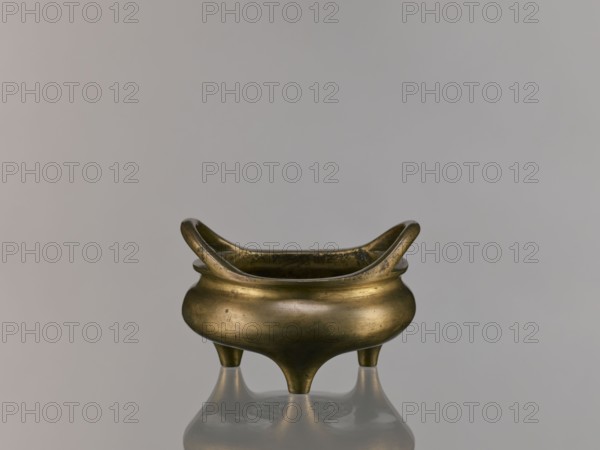 Li-type incense burner, Li-type vessel, Qing dynasty 1644–1911, 18th century China; ceramic vessel/ceremonial ritual incense burner with fantastical beasts; backdated signatures; height 7.5 cm, width 12.1 cm., A small metal vessel with a rounded body and a curved, flaring rim sits centered on a reflective surface; the vessel has a warm brass color with darker patina spots and subtle surface marks, and it stands on three short tapered legs that cast reflections below, set against a smooth pale gray background.