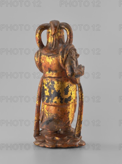 Guardian of Heaven and Defender of the Faith, unknown sculptor, figurine, Southeast Asian art, musical instruments, Southeast Asian culture, guardians, Vietnamese culture, full wood carving, 18th/19th century, Vietnam Vietnamese–Cambodian border, sculpture, height 33.7 cm, A small standing figurine shown from the back on a plain light gray background, with a worn surface showing patches of bright gold, dark brown, and black; the figure wears a long robe with a draped sash and has a rounded headdress with looped elements, and stands on a carved base that is mottled in gold and brown.