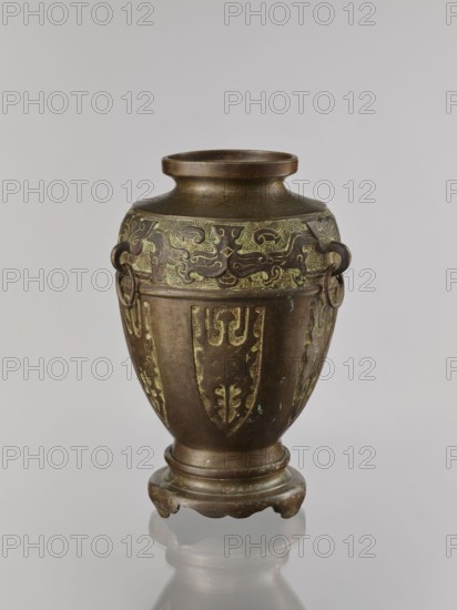 Vase on base;, purchase provenance; Chinese; Qing dynasty 1644–1911; ceremonial vessel with dragons and taotie iconography; early 20th century; China; vessel; height 29.5 cm, diameter 18.7 cm, A bronze vase with a rounded body and flared neck sits on a small decorative foot; the surface shows a brown patina with areas of greenish verdigris and lighter green highlights in raised decorative patterns, and the body is ornamented with several vertical panels of stylized motifs and a band of intricate meandering designs near the shoulder, with two ring handles attached at the upper sides.