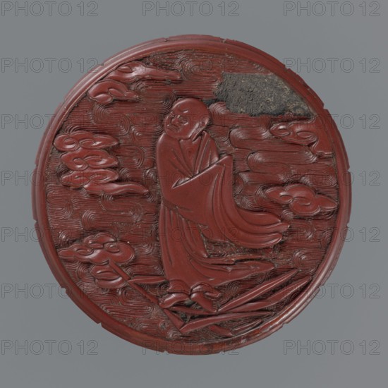 Box with lid; Chinese; Qing dynasty 1644–1911; 19th century. Red lacquer with carved pattern depicting reeds, meander leiwen ornament, clouds and Buddhist motifs. Vessel with lid: lid height 2.3 cm, diameter 8.8 cm; vessel height 3.5 cm, diameter 8.9 cm; base height 1.8 cm, diameter 8.8 cm; box height 3.1 cm., A round carved object mostly in a deep red color with a few areas of dark brown and black, showing a raised figure of a robed person standing with flowing drapery, surrounded by swirling carved cloud-like forms and textured linear patterns, with a smooth raised rim and some worn or chipped sections along the edge.