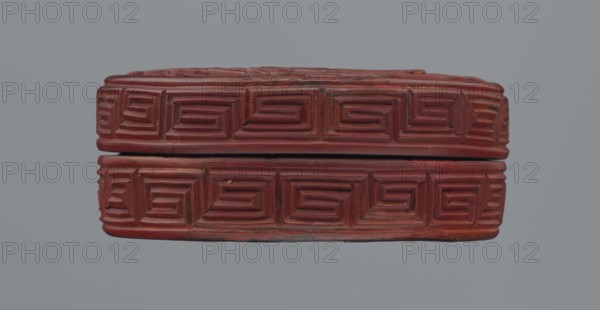 Box with lid; Chinese; red lacquer carved with meander leiwen, cloud and Buddhist ornament; reeds motif; Qing dynasty 1644–1911, 19th century; materials: red lacquer, carved; vessel with lid — lid: H 2.3 cm, dia. 8.8 cm; base: H 1.8 cm, dia. 8.8 cm; box: H 3.1 cm; overall H 3.5 cm, dia. 8.9 cm., A rectangular carved box with a lid is centered against a plain gray background; the box is a deep reddish-brown color and features a repeating geometric carved pattern of concentric rectangular grooves on its visible sides, with a narrow horizontal gap where the lid meets the base; the surface shows slight wear and small chips, and the overall shape is slightly rounded at the corners.
