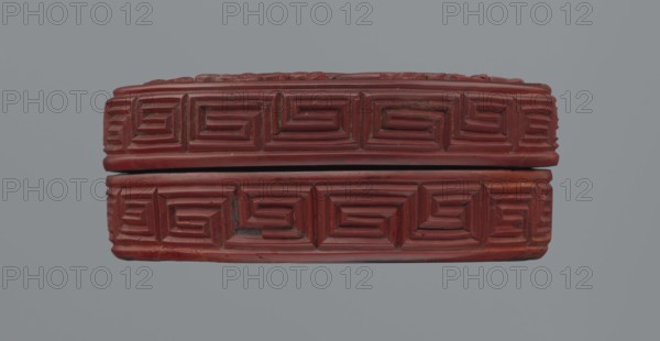 Box with lid, Chinese, Qing dynasty 1644–1911, 19th century. Red lacquer with carved pattern of reeds, meander leiwen, and clouds; Buddhist iconography. Dimensions: lid height 2.3 cm, diameter 8.8 cm; overall height 3.5 cm, diameter 8.9 cm; base height 1.8 cm, diameter 8.8 cm; box height 3.1 cm., A rectangular carved object shown from the side with a visible seam between two stacked parts, featuring a repeating geometric raised pattern across both pieces; the carved surface appears primarily red with darker red and reddish-brown variations and small areas of darker grayish discoloration, set against a plain muted light gray background.
