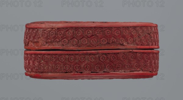 Box with lid;, Two-tone lacquer red exterior, black lacquer interior. Decorated with floral ornament: peonies, bamboo, peaches; kikko geometric pattern. Qing dynasty 1644–1911, 19th century, China. Container box: overall height 3.8 cm; base: height 2.1 cm, diameter 8.8 cm; lid: height 1.8 cm, diameter 8.8–8.9 cm., A carved oval object in shades of red with a textured band of repeating hexagonal floral motifs around its middle, showing a seam where two halves meet; the surface has areas of wear and roughness and slight cracks, and the background is a flat gray.