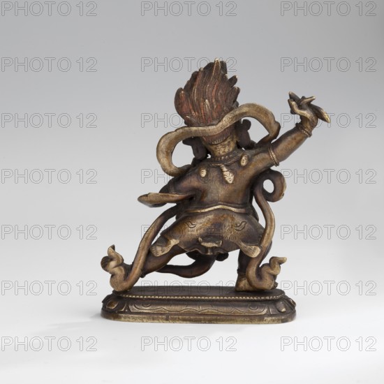 Hayagriva;, purchase provenance; Buddhist art; Himalayan/Tibetan Buddhist art; dharmapala iconography; 2nd half of the 18th century ; Tibet; sculpture, figurine; height 7.0 cm; width 6.1 cm; depth 2.4 cm, A small sculptural figure viewed from the back standing on an ornate base, primarily metallic gold and bronze with darker brown patina; the figure has a stylized flame-like headdress with reddish-brown and gold tones, flowing ribbon-like elements curling around the body in gold and brown, a skirt or garment with textured surface in bronze and gold, and limb and hand details ending in curled decorative shapes. The base shows engraved decorative patterns in gold and dark brown. The background is a smooth gradient of light gray to off-white.