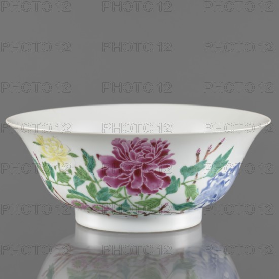 Bowl., Gift; rocks. Chinese art; ceramics. Decorated with peonies in colored overglaze enamels on white porcelain with transparent sintered glaze. Qing dynasty, Yongzheng period 1723–1735. Semicircular body widening toward the upper edge. Porcelain vessel. Height 7.6 cm; diameter 19.5 cm., A white porcelain bowl with a flared rim and a short foot sits against a gray background, decorated around its exterior with painted floral motifs including a large deep pink flower, a yellow bloom, a blue flower, and surrounding green leaves and brown stems; the bowl and its decoration reflect faintly on the glossy surface beneath it, and the interior of the bowl is plain white.
