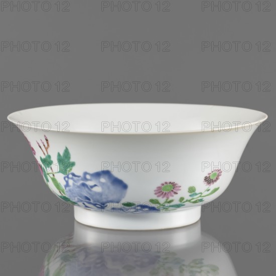 Bowl. Semicircular body widening toward the upper edge. Porcelain body with white, transparent, sintered glaze; decoration painted with overglaze enamel paints depicting peonies and floral decorations in colored porcelain. Chinese, Qing dynasty, Yongzheng period 1723–1735. Height 7.6 cm; diameter 19.5 cm., A white porcelain bowl with a flared rim and a short foot sits against a gray background, decorated around its exterior with floral and foliage motifs in colors including green, blue, pink, and a touch of brown, and the bowl is reflected faintly on the glossy surface below.