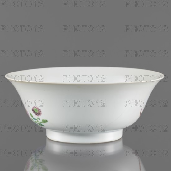 Bowl. Semicircular body widening toward the upper edge. Porcelain body with white, transparent, sintered glaze; decoration painted with overglaze enamel paints depicting peonies and floral motifs. Colored porcelain, Qing dynasty Yongzheng period, 1723–1735, China. Height 7.6 cm; diameter 19.5 cm., A white porcelain bowl with a flared rim and a short foot sits on a reflective surface, showing a faint reflection underneath; the bowl has delicate painted floral motifs in shades of pink and green on its exterior and a thin pale gold or cream line along the rim, with the background appearing neutral gray.