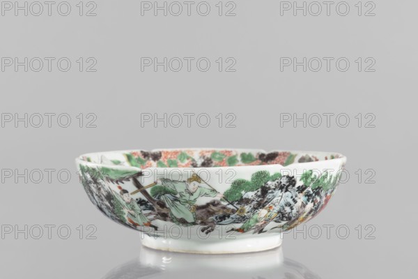 Bowl., Chinese; Qing dynasty 1644–1911. 19th century. Porcelain body with white, transparent glaze; decoration painted with overglaze enamel paints and iron red depicting figural and knightly scenes. Six-leafed belly form. Height 6.5 cm; diameter 20.0 cm; weight 0.75 kg., A shallow porcelain bowl with a scalloped rim sits on a reflective surface; the bowl is primarily white and decorated around its exterior with painted scenes in green, black, brown, orange, and touches of yellow, showing a group of human figures in flowing garments, stylized trees and foliage, and rocky landscape elements; the interior rim also has painted floral and foliage motifs in green, orange, and black.