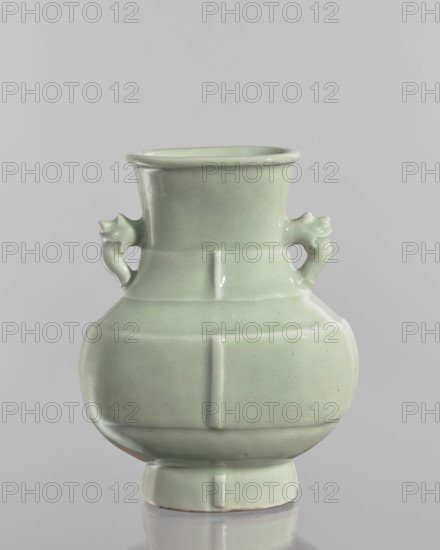 Vase, celadon glaze, Chinese, ceramic decorative vessel in Qianlong style Qing dynasty, 1736–1795. Decoration with vertical, plastic narrow stripes on the foot, body, and neck. Vessel; height 20.5 cm, width 16.4 cm, depth 6 cm., A pale green glazed ceramic vase with a rounded body tapering to a narrower neck and flared rim, featuring a pair of small sculpted handles shaped like stylized animal heads on opposite sides, subtle vertical and horizontal raised bands creating segmented panels, a slightly raised circular foot, and a smooth glossy surface against a neutral light gray background.