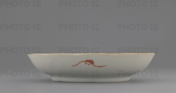 Plate. Chinese porcelain fragment, Qing dynasty 1644–1911, 19th century. White glaze with overglaze enamel painted decoration depicting cranes and waves. Vessel, height 2.8 cm, diameter 13.5 cm, weight 0.15 kg. Maker and specific, A shallow ceramic dish with a scalloped rim sits on a flat surface; the dish is principally white with a thin golden edge along the rim and a simple reddish-brown brushstroke motif on its side. The background and surface are shades of gray, and the dish casts a soft shadow beneath it.
