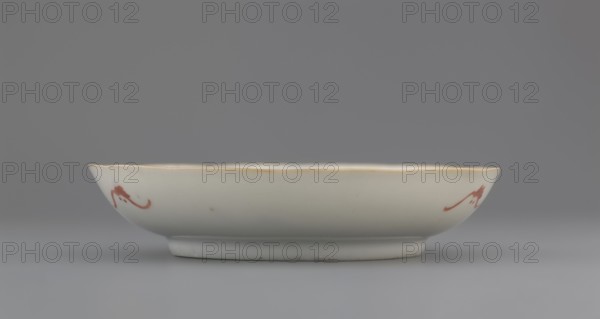Plate. Porcelain fragment with white glaze; decoration painted with overglaze enamel paints depicting cranes and waves. Chinese; Qing dynasty 1644–1911. 19th century. Vessel. Height 2.8 cm; diameter 13.5 cm; weight 0.15 kg., A shallow ceramic bowl seen from the side, with an off-white surface and a subtle glossy finish, a rim edged in a warm yellowish-beige tone, and a few small red brushstroke decorations on the exterior; the bowl sits on a short footring and is set against a smooth gray background showing varying shades of gray.