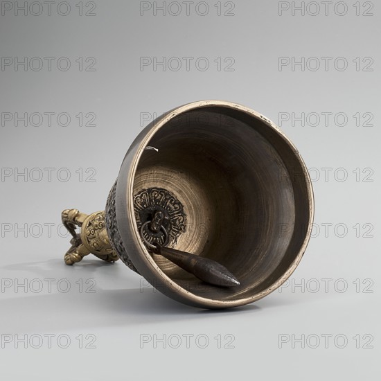 Bell, Tibetan Buddhist art, Himalayan art, Mongolian art, Himalayan culture, Mongolian culture, vajras, musical instrument, percussion instrument, idiophone, used in religious rites, ritual object, late 18th century, Mongolia place of origin, ceremonial object, height 15.7 cm, diameter 8.2 cm, A metal bell lies on its side showing its interior and a decorative handle, with a dark metallic clapper resting inside; the bell and handle display a mix of brass and bronze tones with darker brown patina and subtle wear, and the background and surface are shades of pale gray.