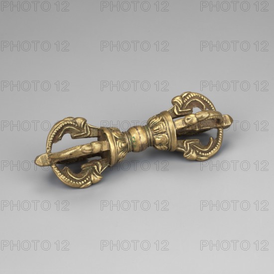 Vajra; creator, Tibetan Buddhist art; Himalayan; vajra; 19th–20th century; possibly Mongolia; ceremonial object; height 9.7 cm; diameter 3.4 cm, A metallic object with a golden color lies on a smooth light gray background; it has a symmetrical double-ended design with a central rounded section and a pair of ornate curved prongs at each end, showing decorative carved ridges and scalloped edges, and small areas of darker greenish discoloration on the metal surface.