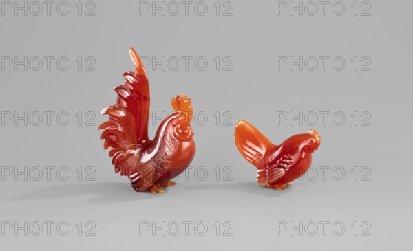 Rooster and Hen; sculptor, Chinese; Qing dynasty 1644–1911; 18th–19th century; sculpture depicting animals—birds, domestic fowl hens and roosters., A group of two carved bird figures made of a translucent orange-red material sit on a flat neutral gray surface against a smooth light gray background, one figure is larger with an upright tail and detailed carved feather textures while the other is smaller with a shorter tail and similar feather carving; both display glossy surfaces with highlights and subtle darker red and amber color variations and cast soft shadows on the surface.