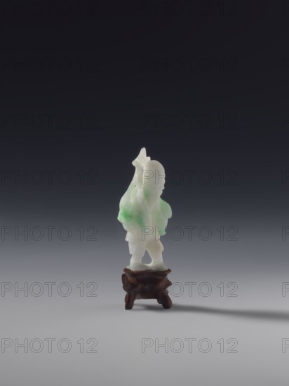 Fisherman with a Basket and a Fish on a Rod, unknown sculptor, fish, fishermen, Chinese art, Chinese culture, Qing 1644–1911, White jade with green spots, solid sculpture, engraved, 19th century, figurine, sculpture, height 7.2 cm, A small carved figurine made of white and pale green stone standing on a dark brown carved wooden stand, set against a gradient background that shifts from dark gray at the top to light gray at the bottom; the figurine has smooth rounded forms and a slightly translucent appearance with patches of green, and the stand has organic curved legs and a polished texture, casting a faint shadow on the surface below.