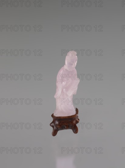 Guanyin on a base, Chinese art, Chinese culture, Qing 1644–1911, Chinese Buddhism, goddess, figurine carved in rose quartz, full sculpture, engraving, 19th century, China, sculpture, figurine, height 6 cm, A small carved figure made of translucent pale pink material stands on a short carved wooden base that is dark brown with a slightly glossy finish; the figure appears robed with smooth flowing contours and has a rounded head and simplified facial features, and the background is a gradient of gray.