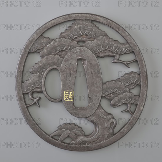 Crossguard tsuba, Sunagawa, Masayoshi, / personal slogans / artist, Sunagawa,  school, Japanese art, Japanese culture, Edo 1603–1868, weapons, melee weapons, swords, katana, sword crossguard, pine trees, bamboos. Round tsuba tatemaru gata with one side hole katahitsu ana, massive rectangular edge kaku mimi closing an openwork positive composition depicting a spreading pine tree with bamboo growing from its thick trunk, marked with a few leaves. Seppa dai oval; the kozuka hitsu ana hole is woven into the decorative motif, although clearly visible. Signed. 1st half of the 19th century Edo period, Japan. Tsuba; height 7.75 cm, width 7.4 cm, thickness 0.5 cm., A round dark gray metal object with a circular outer rim and an openwork interior showing sculpted cloudlike shapes and tree-like forms, including a stylized trunk and branches; the metal has a slightly rough, weathered texture with lighter gray highlights and small areas of wear; a small patch of bright gold color appears near the c...